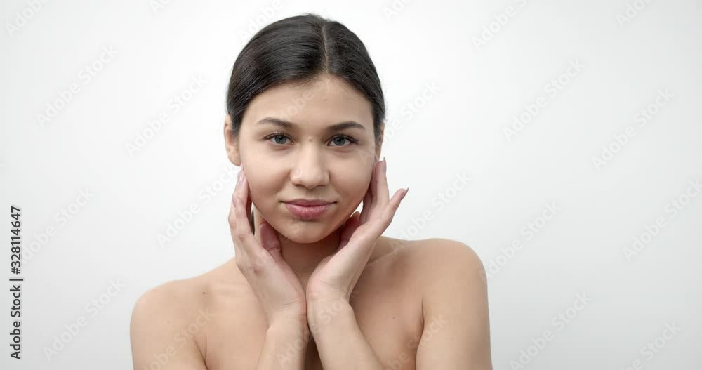 Attractive lady with dark hair and clean skin holding hands near face and looking at camera with white background. Concept of natural beauty and tenderness Attractive lady with dark hair and clean skin holding hands near face and looking at camera with white background. Concept of natural beauty and tenderness