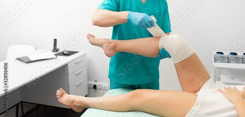 Traumatologist bandaging damaged knee of a woman with an elastic bandage.