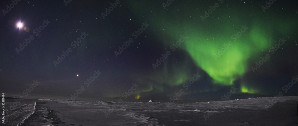 Auroras (Northern Lights) and full moon over the frozen tundra of Nunavik (Canada) in winter