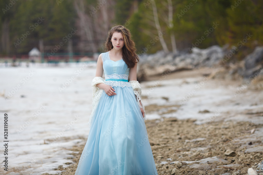 A girl in a blue magnificent dress nullifies on the seashore.