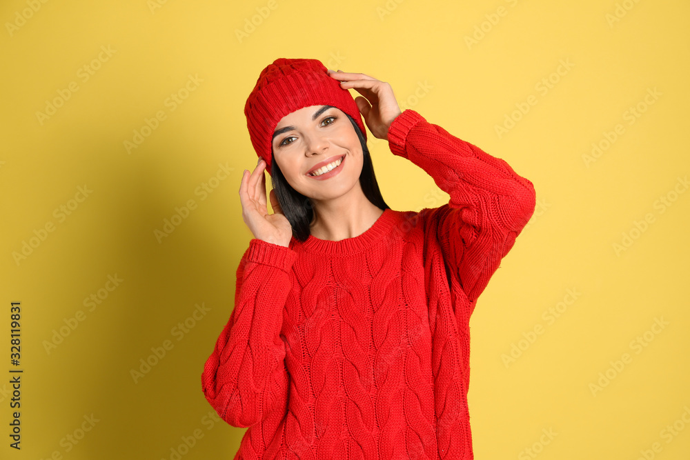 Young woman wearing warm sweater and hat on yellow background. Winter season