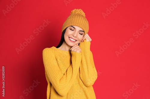 Young woman wearing warm sweater and hat on red background. Winter season © New Africa