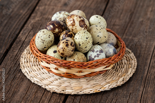 Quail eggs in a wicker basket on a wooden background.