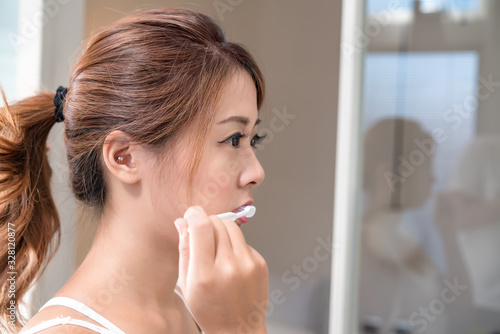 Beautiful young girl brushing teeth in front of her bathroom mir