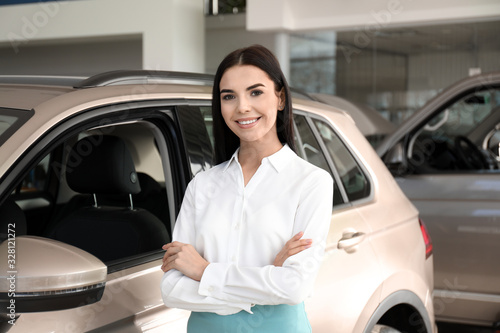 Young saleswoman near new car in dealership