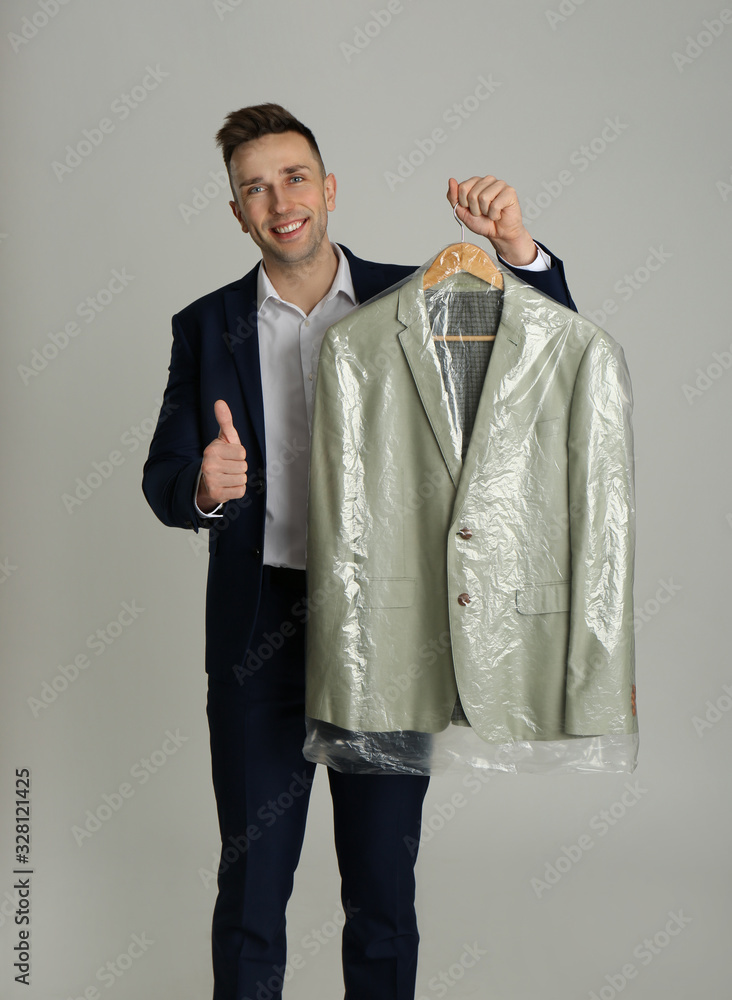 Man holding hanger with jacket in plastic bag on light grey background. Dry-cleaning service Man holding hanger with jacket in plastic bag on light grey background. Dry-cleaning service
