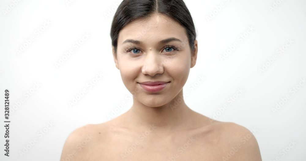 Front view of charming lady with dark hair and blue eyes looking directly at camera while posing in studio with white background. Pretty woman with natural beauty and bare shoulders. Front view of charming lady with dark hair and blue eyes looking directly at camera while posing in studio with white background. Pretty woman with natural beauty and bare shoulders.
