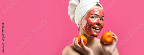 Fototapeta Naklejka Na Ścianę i Meble -  Beauty portrait of woman in white towel on head with red nourishing mask on face. Skincare cleansing eco organic cosmetic spa relax concept. A girl stands with her back holding an orange mandarin.