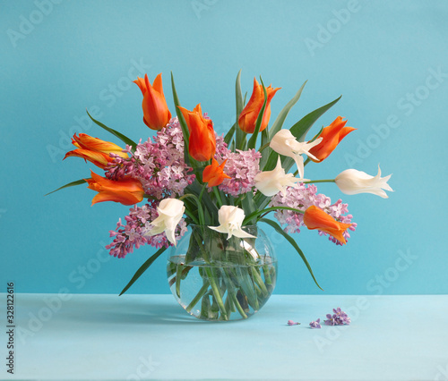 Bouquet of flowers  tulips and lilac on glass vase. Spring blue background. 8 of March or celebration concept