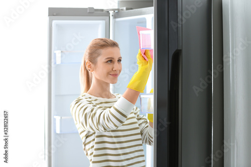 Woman in rubber gloves cleaning empty refrigerator with rag at home