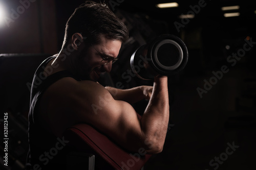 A handsome man with glasses doing an exercise for biceps with a barbell. The guy is engaged in bodybuilding. Trainer in the gym with muscular arms.