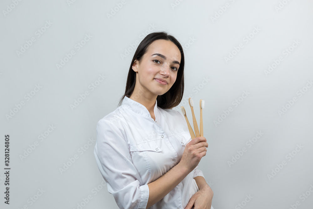 A young brunette girl holds an ecological toothbrush in her hands. A girl in a white coat promotes zero waste. A young brunette girl holds an ecological toothbrush in her hands. A girl in a white coat promotes zero waste.