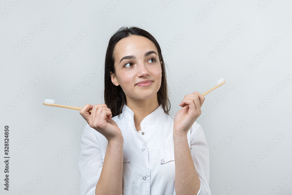 A young brunette girl holds an ecological toothbrush in her hands. A girl in a white coat promotes zero waste. A young brunette girl holds an ecological toothbrush in her hands. A girl in a white coat promotes zero waste.