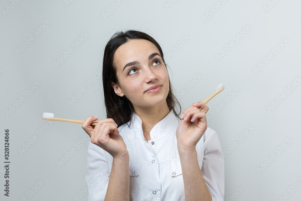 A young brunette girl holds an ecological toothbrush in her hands. A girl in a white coat promotes zero waste. A young brunette girl holds an ecological toothbrush in her hands. A girl in a white coat promotes zero waste.