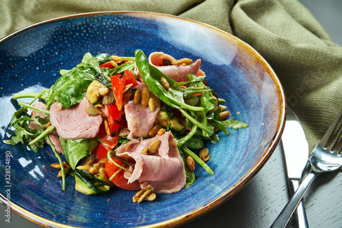 Appetizing warm salad with veal grill and vegetables, spinach and pine nuts in a blue bowl on wooden background. Healthy eating. Close up, copy space, selective focus