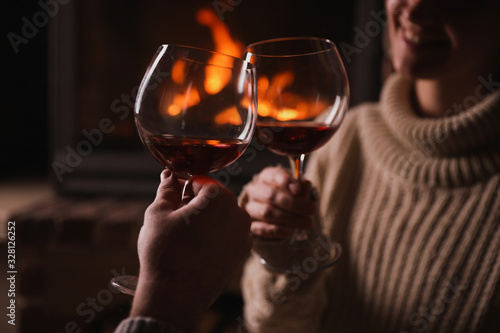Bild auf Leinwand Couple with glasses of red wine near fireplace, closeup