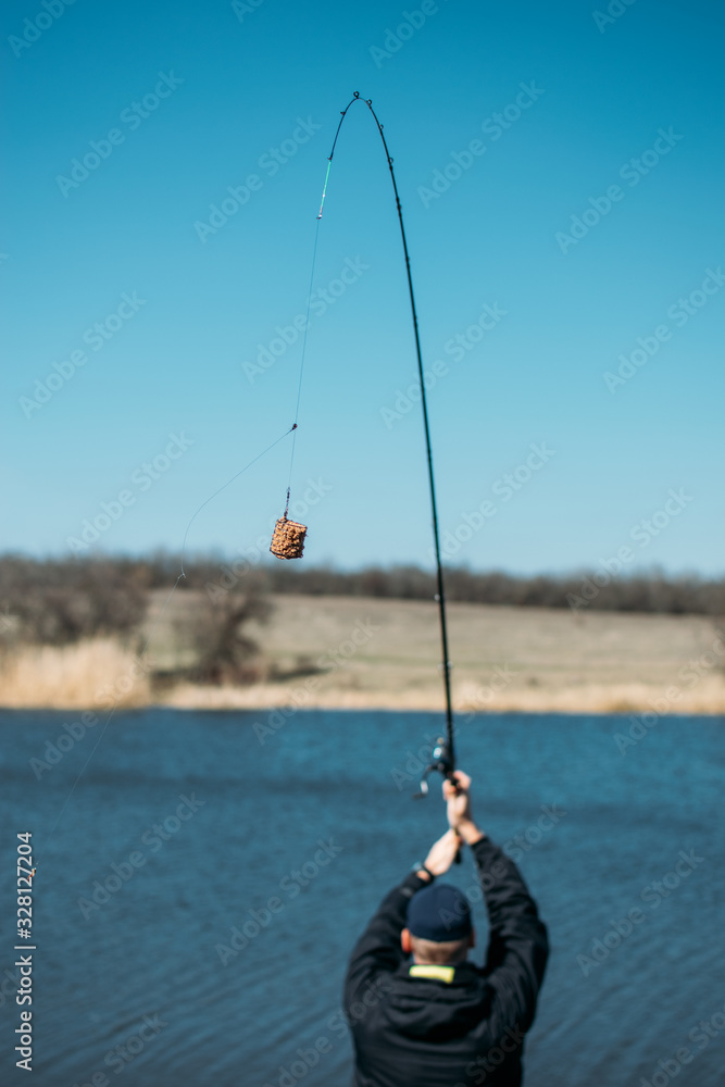 Feeder fishing. Carp Fishing Steel Basket Bait Feeder on rod close up. Male fisherman fishing at sun day on the lake