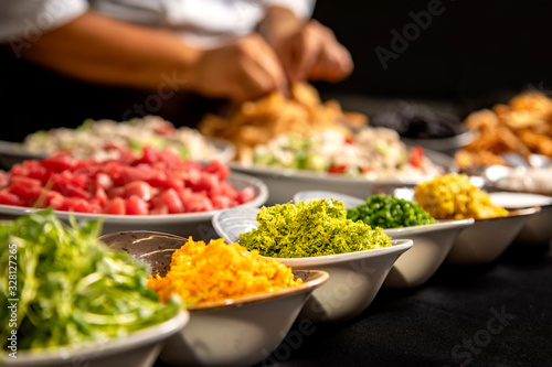 Rows of ingredients and spices in a bowl with chefs hands diffused in the background