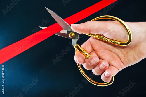 Hand cutting the red ribbon with scissors.