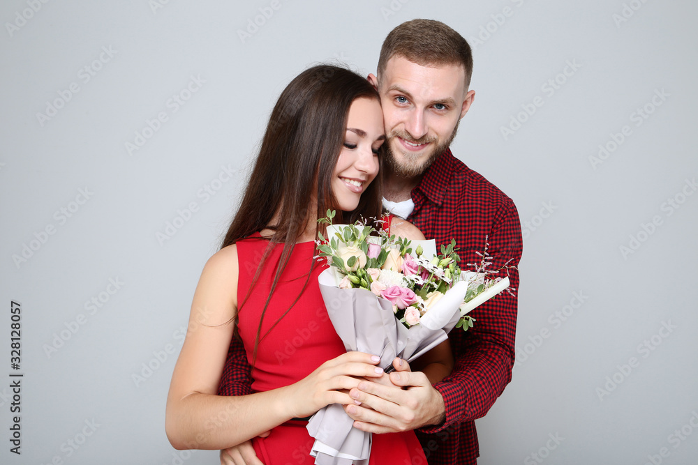 Happy young couple with bouquet of flowers on grey background Happy young couple with bouquet of flowers on grey background