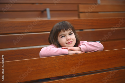 a little cute girl of Asian appearance 7 years old sits in a park breathing fresh air on a bench alone