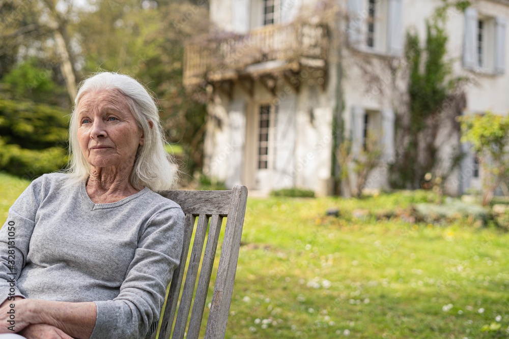 Thoughtful senior woman sitting on wooden chair in garden Thoughtful senior woman sitting on wooden chair in garden