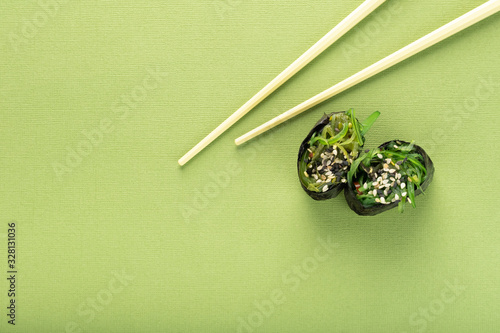 Two Chuka seaweed Sushi with chopsticks on a green background, top view