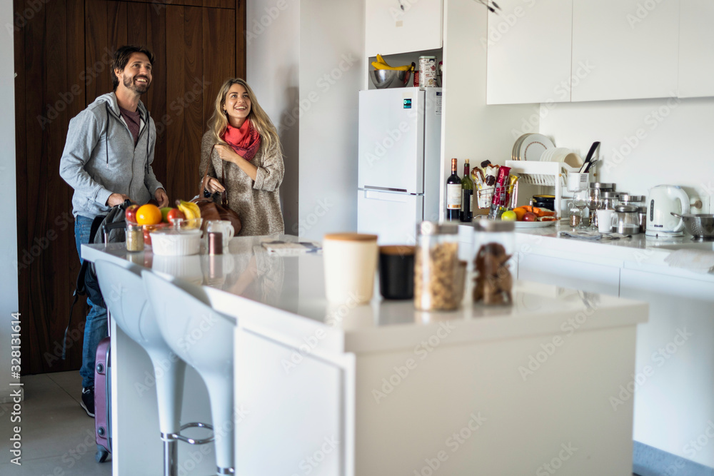 Happy young couple entering in kitchen at new home with luggage Happy young couple entering in kitchen at new home with luggage