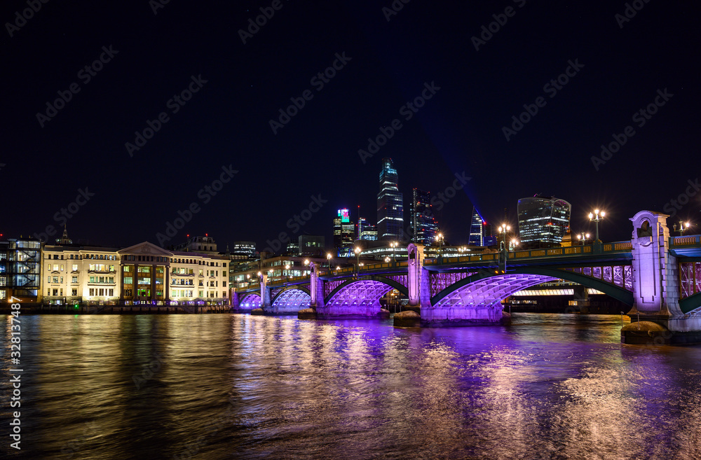 City of London, UK with view over the River Thames and Southwark Bridge at night. Cityscape with skyscrapers, lights, and dark sky. London 2020.
