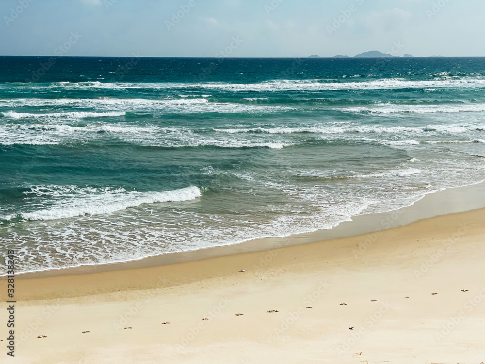 Sandy seashore, calm soft waves at sea, sunny weather, blue sky with white clouds Sandy seashore, calm soft waves at sea, sunny weather, blue sky with white clouds