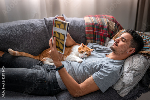 gato blanco y marrón se duerme sobre su dueño que lee recostado en un sofá debajo de la ventana