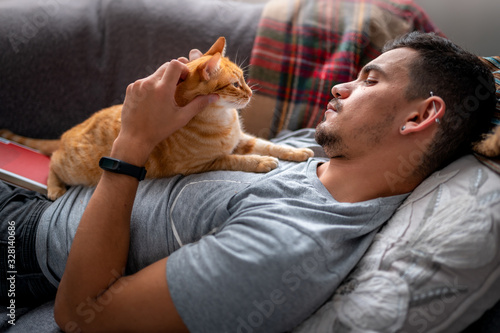 gato atigrado se encuentra en el pecho de un joven tumbado en el sofá debajo de la ventana