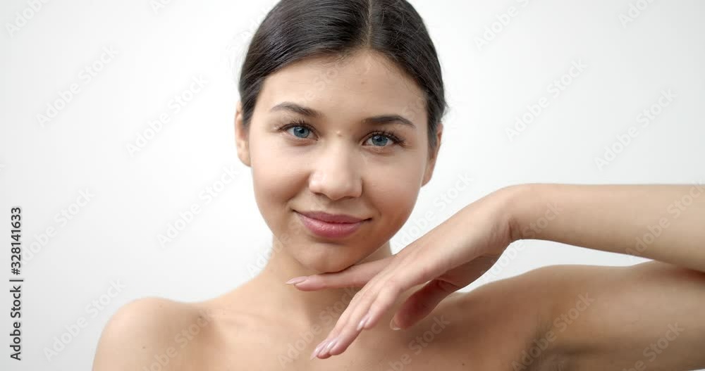 Beautiful woman with natural makeup and dark hair holding her hands near naked shoulders over white background. Female model with blue eyes posing in studio Beautiful woman with natural makeup and dark hair holding her hands near naked shoulders over white background. Female model with blue eyes posing in studio