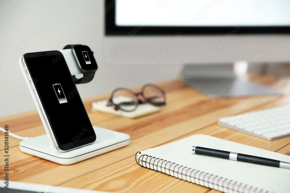 Mobile phone and smartwatch with wireless charger on wooden table. Modern workplace accessory Mobile phone and smartwatch with wireless charger on wooden table. Modern workplace accessory