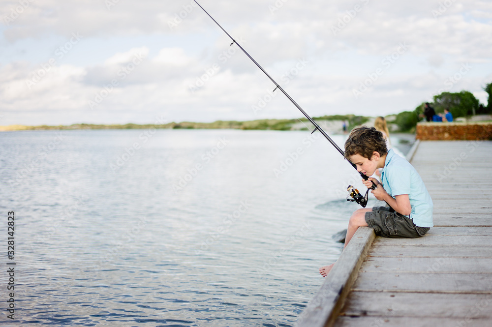 Young boy holding a fishing rod and sitting on a wooden dock Young boy holding a fishing rod and sitting on a wooden dock