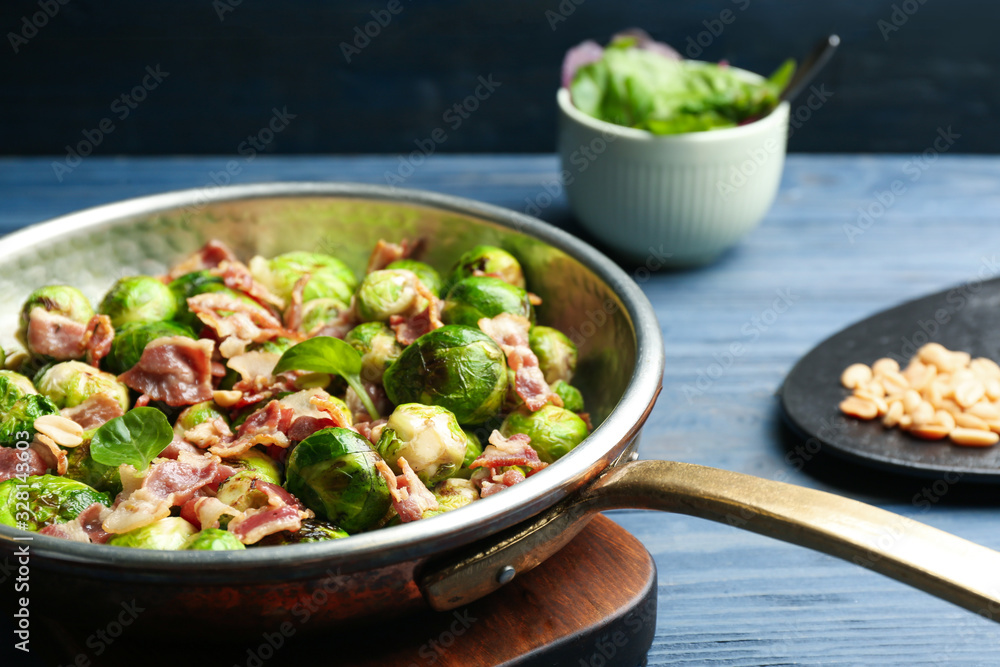 Delicious Brussels sprouts with bacon in frying pan on blue table, closeup