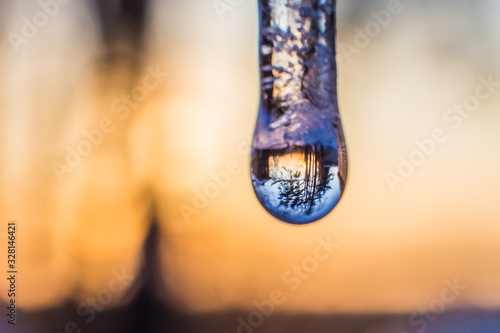 the surrounding nature is beautifully reflected in a drop of water on an icicle