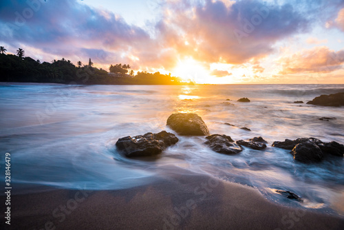 BeautifulTropical Island Paradise of Colorful Pastel Sunrise Sky at Dawn with Sun Coming Over Ocean Horizon on Sandy Beach with Smooth Water and Mountain Background and Pink Clouds on Maui Hawaii