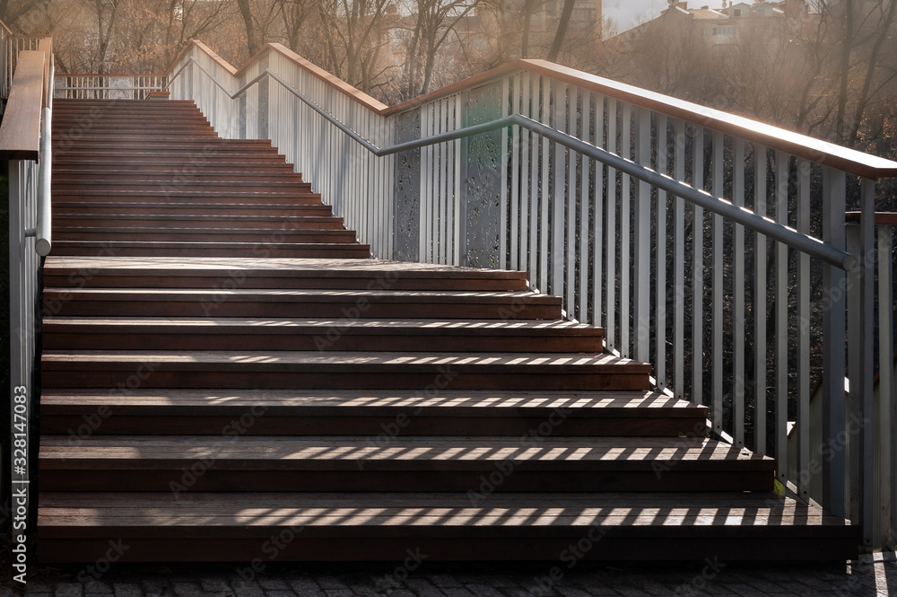 Staircase with a shadow. Close-up staircase with wooden steps and metal railing. A play of light and shadow in the evening. Staircase with a shadow. Close-up staircase with wooden steps and metal railing. A play of light and shadow in the evening.