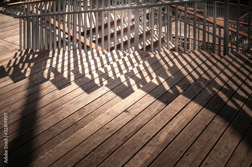Staircase with a shadow from the railing. Close-up staircase with wooden steps and metal railing. A play of light and shadow in the evening. © Alex Puhovoy