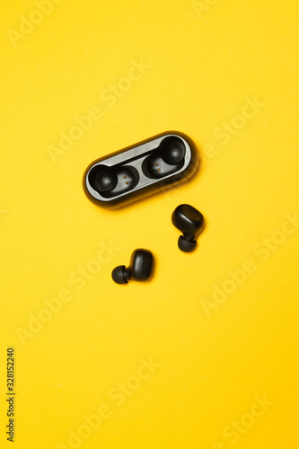 Modern technologies of the future. Black plastic wireless headphones on a yellow background, top view, flat lay. Vertical photo. Wireless connection.