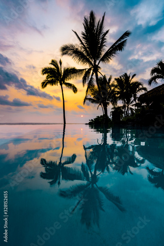 Scenic Tropical Island View with Colorful Sunset and Silhouette Palm Trees Reflection on Crystal Clear Blue Infinity Pool in Hawaii