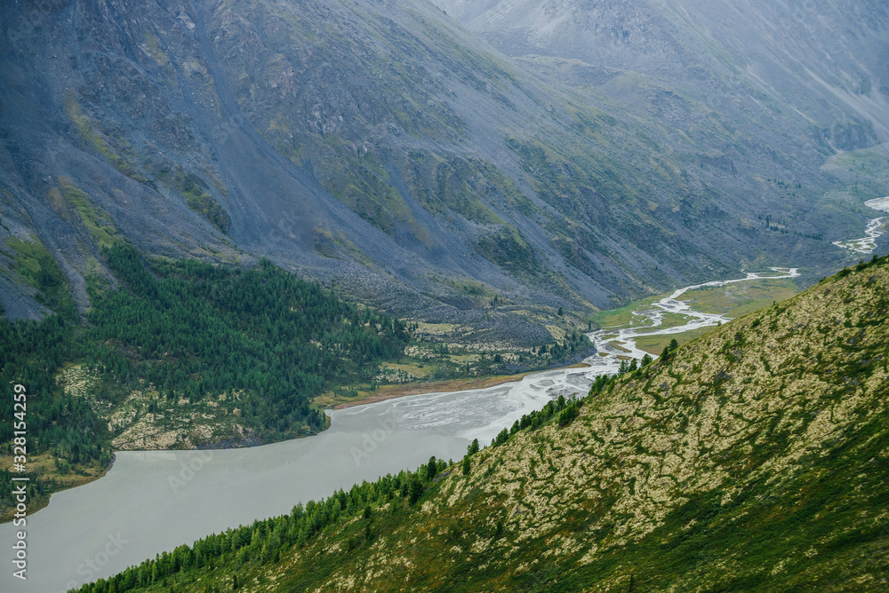 Atmospheric alpine scenery with beautiful valley with mountains lake and giant textured hillside with nature patterns. Awesome aerial view to big rocky hills and huge mountains. Trees on mountainside. Atmospheric alpine scenery with beautiful valley with mountains lake and giant textured hillside with nature patterns. Awesome aerial view to big rocky hills and huge mountains. Trees on mountainside.