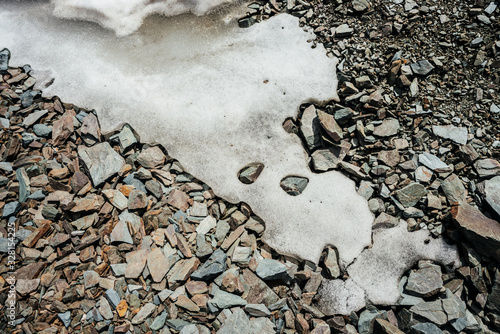 Nature background of snow on chaotic pile of stones. Natural backdrop of ice on random boulders. Firn on combe rock close-up. View from above to snowy boulder stream. Minimalist texture of stony heap.
