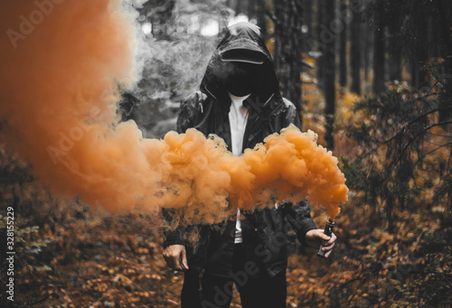 Colorful Abstract Photo Concept Idea with Man Holding Orange Smoke Bomb Wearing Black Jacket and Face Blacked Out Inside Damp Wet Moody Dark Forest Scene  photo