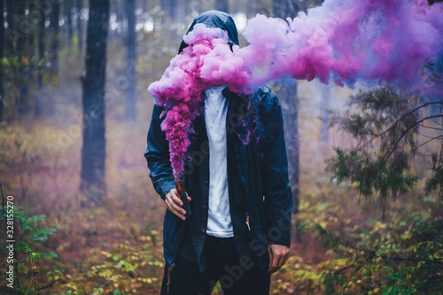 Colorful Abstract Photo Concept Idea with Man Holding Smoke Bomb with Pink Purple Blue Smoke Covering His Face Inside Damp Wet Moody Forest Scene  photo