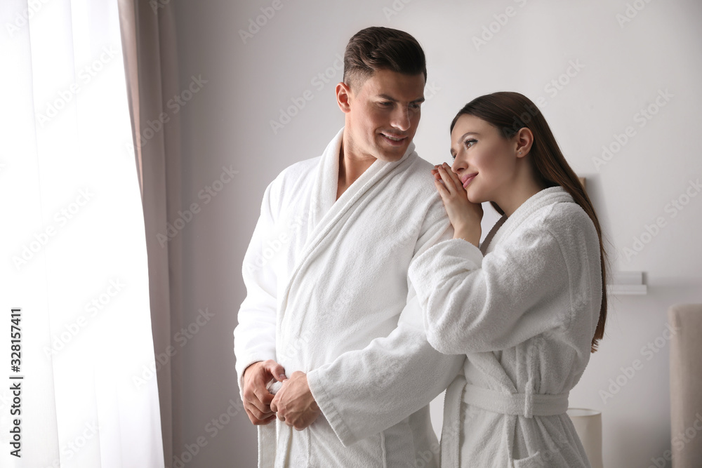 Happy couple wearing bathrobes near window in room Happy couple wearing bathrobes near window in room