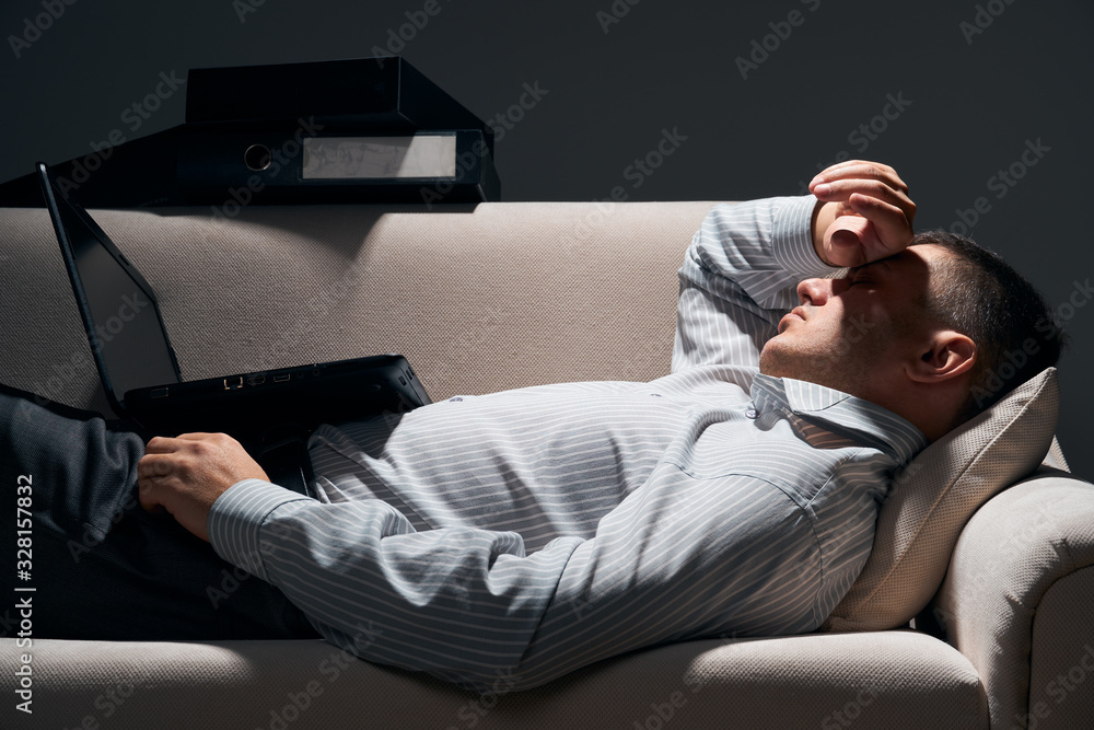 Fototapeta premium businessman is lying on the sofa with laptop and resting