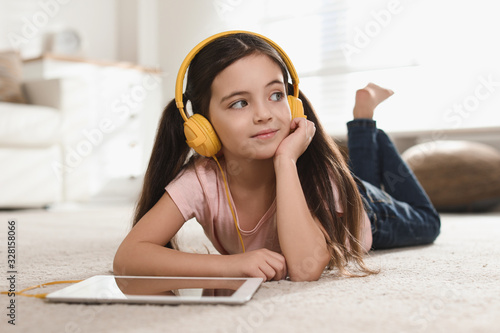 Cute little girl with headphones and tablet listening to audiobook at home