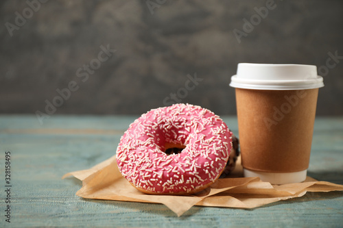 Yummy donuts with sprinkles and paper cup on wooden table photo